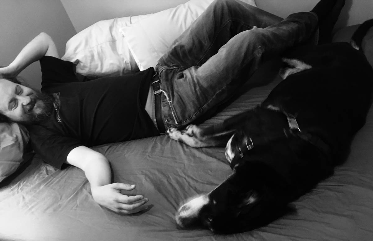 Bessie the big black dog lazing on the bed with her human